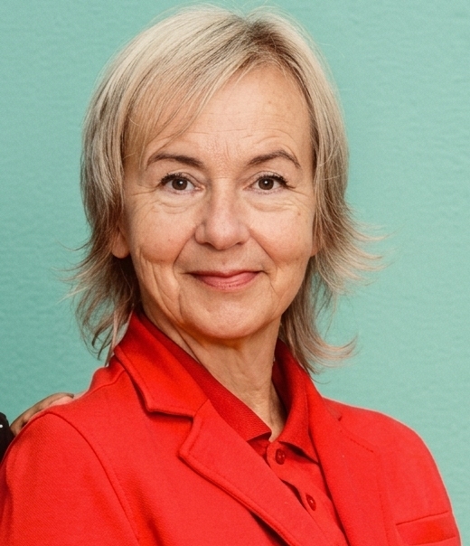 Freundliches Porträt von Claudia mit kurzen, hellblonden Haaren und rotem Blazer, lächelnd vor türkisfarbenem Hintergrund.
