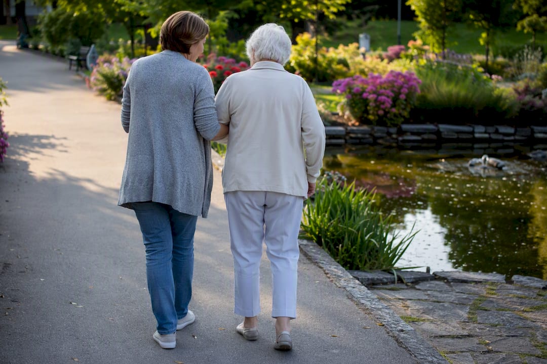Pflegekraft unterstützt ältere Frau beim Gehen vor der Klinik