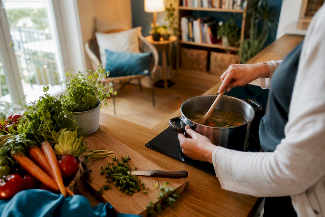 Pflegekraft rührt im Topf in der Küche eines Senioren